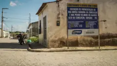 Placa que anuncia obra de pavimentação em uma rua com pedras do tipo paralelepípedo