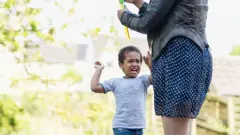 Criança fazendo birra ao lado da mãe