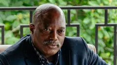 Une photo en buste de Joseph Kabila. Il porte une veste bleue et une chemise bleue à carreaux, dont le col est ouvert.