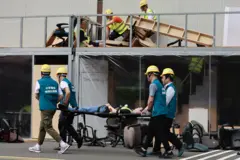 Pessoas usando capacetes de segurança e coletes carregando uma pessoa em uma maca