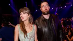 Taylor Swift usa um vestido prateado com pedrarias, enquanto Travis Kelce veste um conjunto todo preto