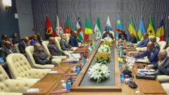 Abategetsi bitabiriye inama isanzwe ya 26 ya CEEAC, i Malabo, muri Guinée équatoriale. Ifoto yatangajwe ku rubuga X n'ibiro bya perezida wa DRC, ku itariki ya 7 Kamena (6) mu mwaka wa 2025. Abategetsi baricaye, imbere yabo hari indangururamajwi n'amabendera mato y'ibihugu, hirya inyuma hari amabendera manini. 