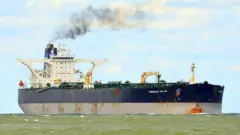 Petroleiro no mar com o letreiro 'Overseas Mulan' pintado em branco contra fundo azul escuro