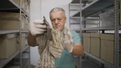 El doctor Arsim Gerxhaliu inspecciona una prenda de vestir encontrada en una de las fosas comunes.