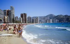 Vista de Benidorm desde la playa, con turistas bañándose y rascacielos.