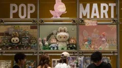 Clientes observam uma vitrine da Pop Mart repleta de bonecos Labubu e outras figuras colecionáveis da série The Monsters, em 16 de junho de 2025, em Chongqing, China