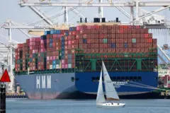 Um veleiro passa por um navio porta-contêineres no porto de Oakland, em Oakland, na Califórnia