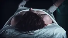 বিছানায় থাকা একটি নারী দেহের ওপর থেকে চাদর সরিয়ে নিচ্ছে গ্লাভস পরা দুটি হাত