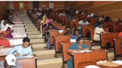 Ọpọ awọn akẹkọ fasiti joko si yara ikawe to ni akasọ, wọn n dori kodo lati kọ iwe