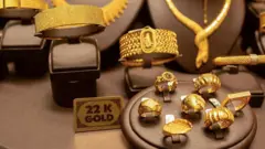 Dois braceletes de ouro (esq.) e sete anéis de ouro. Entre eles, um letreiro dizendo 'ouro 22 quilates'