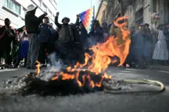 Un fuego pequeño en la calle y detrás hay varias personas paradas manifestando