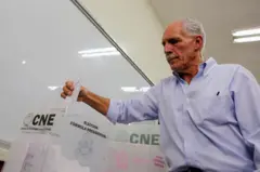 Nasry "Tito" Asfura coloca su voto en la urna del CNE. Detrás se ve un pizarrón de aula escolar.