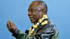 Cyril Ramaphosa, vêtu d'une veste en cuir vert, jaune et noir et portant une guirlande de roses jaunes et blanches autour du cou, fait des gestes de la main pendant qu'il parle.