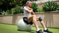 Eric Topol con lo brazos cruzados en el pecho sentado en una pelota de Pilates