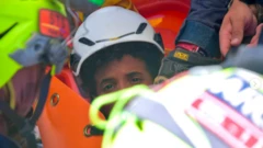 La foto muestra la mitad del rostro de un chico, el resto está oculto por los rescatistas. Lleva un casco blanco y tiene el pelo oscuro y rizado