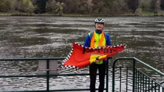 Nikola Boca segurando a bandeira da Ferrari perto de um rio a caminho de Estrasburgo