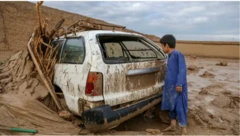 عکسی از سیلاب ویرانگر در افغانستان. پسری به یک موتر گیر مانده در گل ناشی از سیلاب میبیند