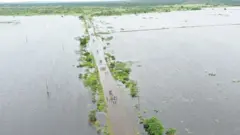Vista aérea mostrando moradores atravessando uma estrada perto de Maputo em meio a enchentes, em 20 de janeiro de 2026.