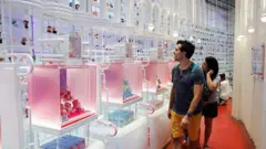 Um homem e uma mulher observam, surpresos, uma parede repleta de bonecos da Pop Mart