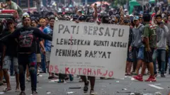 Seorang pria sedang mengangkat poster lengserkan bupati pati.