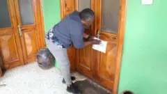 Umugabo urimo gushyira itangazo ku muryango w'inzu