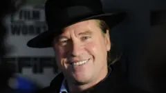 2012 picture of Kilmer wey wear black hat and dey smile into di camera