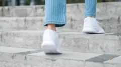 Unos pies con calzado deportivo blanco subiendo escalones en lugar indefinido