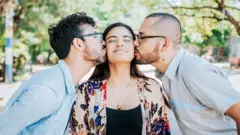 Dois jovens beijando a bochecha de uma mulher