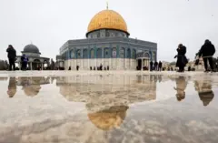 قبة الصخرة وانعكاس لها على الأرض التي تبدو مبتلة، وعدد من الأشخاص حولها