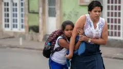 Una madre acompaña al colegio a su hija, que carga una mochila.