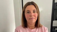 Michelle Sneddon veste uma camiseta rosa e olha para a câmera. Ela tem cabelos castanhos na altura dos ombros.