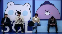 Quatro homens sentados em uma fileira em uma área pública de estar em uma estação de metrô, mexendo em seus celulares em Seul, em 8 de abril de 2025.