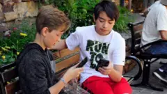 Dos niños sentados mirando sus teléfonos
