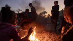 چند کودک فلسطینی که دور آتش در نور غروب جمع شده‌اند