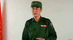 စစ်စိမ်းရောင်ဝတ်စုံကိုဝတ်ဆင်ထားပြီး မတ်တပ်ရပ်အနေအထားနဲ့စကားပြောနေတဲ့ ကိုးကန့်တပ်ခေါင်းဆောင် ဖုန်တာရွှင် ကိုတွေ့ရပါတယ်။ 
