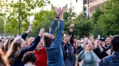 Personas en Róterdam alzan los brazos para alcanzar los marcapáginas con poemas que caen del cielo