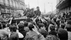 La gente en las calles rodeando a un tanque con soldados.