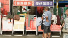 Um homem de camiseta e shorts olha para uma fileira de murais vermelhos e amarelos com anúncios de emprego e roupas por cima.