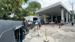 ඉන්ධන පිරවුම්හලක යතුරුපැදිකරුවන් විශාල පිරිසක් සිටින අතර ත්‍රීරෝද රථයක්ද තිබේ.