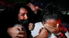 Un grupo de familiares y amistades reaccionan durante un operativo de rescate en La Guaira, Venezuela. Un hombre abraza a una mujer visiblemente conmocionada y otra se cubre la cara con la mano llorando. 27 de junio 2026