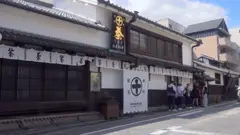 道路に面した和風の建物。白壁に茶色の格子、かわらのひさしや屋根。そこに、丸に十字の紋や「中村銘茶」「茶」といった文字が書かれた、白いのれんや幕がかかっている。ひさしの上には茶色い板に金で「茶」と書かれた看板も立つ。店の前に数人の行列ができている