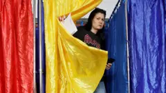 Женщина выходит из кабинки для голосования, задрапированной румынским флагом