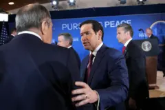 Lavrov aparece de costas para a câmera; Rubio fala com ele, tocando seu ombro. O secretário de Defesa dos EUA, Pete Hegseth, está atrás deles diante de um painel com a frase “Pursuing peace” (“Buscando a paz”, em tradução livre), em Anchorage, no Alasca, em 15 de agosto de 2025.