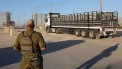 ضابط إسرائيلي ينظر إلى شاحنة محملة بالمساعدات الإنسانية وهي تدخل قطاع غزة عبر معبر بيت حانون (معبر إيرز)