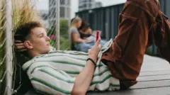 地面に横たわり、スマートフォンを手に持って画面をスクロールしている若い男性の写真