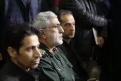 O brigadeiro-general Esmail Qaani sentado entre dois outros homens, olhando para frente, com um feixe de luz iluminando seu rosto, em uma cerimônia fúnebre no dia 17 de fevereiro de 2026