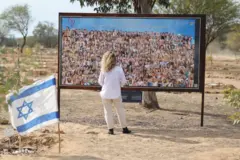 አንዲት ሴት በጥቅምት ሰባቱ ጥቃት የተገደሉ እስራኤላዊያንን ምስል ከያዘ ቢልቦርድ ፊት ቆማ 