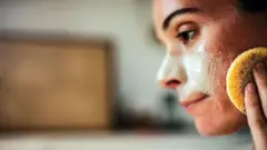 Mulher jovem passando creme no rosto com esponja