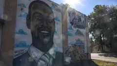 レンガの壁に黒人男性の似顔絵と名前のグラフィティなどが描かれている