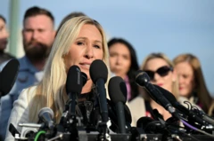 Marjorie Taylor Greene fala em uma conferência de imprensa ao ar livre. Vários microfones grandes estão agrupados na frente dela.